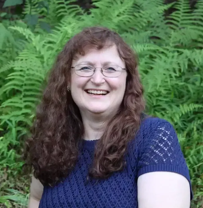 Cheri sitting in front of a backdrop of ferns smiling